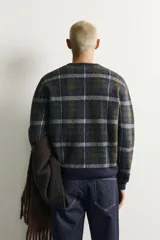 Jersey de punto con lana, de corte relajado, cuello redondo y manga larga. Presenta un diseño de cuadros en tonos oscuros con acabados en rib en cuello, puños y bajo.