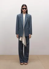 Blazer Uma de corte sastre en color azul acero, confeccionado en mezcla de lana, poliéster y elastano, con forro interior de viscosa. Presenta solapas de muesca, hombreras marcadas, bolsillos con solapa y cierre frontal de doble botonadura.