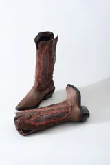 Bota texana de cuero negro con apliques de cuero marrón en los laterales y pespuntes en color crema. De caña media/alta y taco bajo. Diseño calado con motivos geométricos.