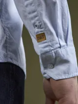 Camisa celeste de corte clásico, confeccionada en tela Oxford de algodón. Tiene cuello abotonado, manga larga con puños abotonados y bolsillo en el pecho. Marca Mersey.