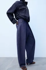 Pantalón confeccionado con lino de tiro alto con pliegues delanteros y cinco bolsillos. Presenta pernera holgada y cierre frontal con cremallera, botón interior y gancho.