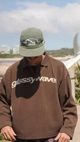 Buzo de tejido de punto color marrón con cuello polo, manga larga y estampado frontal con el nombre de la marca en color crema.