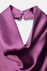 Top halter confeccionado en tejido satinado de color lila, con escote fluido y hombros descubiertos. Presenta cierre en la espalda con botón oculto.