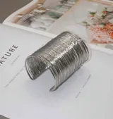 Brazalete ancho plateado con diseño de alambre enrollado.