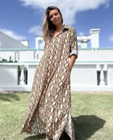 Vestido camisero largo con estampado de piel de serpiente en tonos marrones y negros. Presenta cuello camisero, cierre frontal de botones, mangas tres cuartos con puños vueltos y aberturas laterales en el ruedo.