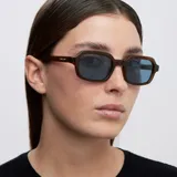 Lentes de sol con armazón marrón traslúcido de diseño cuadrado con bordes redondeados y lentes celestes.