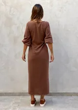 Vestido largo color verde militar, con cuello redondo, mangas largas abullonadas con puños elásticos y detalle de lazo anudado en la cintura. Presenta una abertura lateral en la falda.