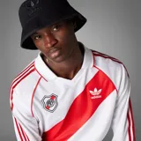 Camiseta de fútbol Adidas de manga larga de River Plate, modelo retro inspirado en 1994. Diseño en color blanco con la tradicional banda roja diagonal, cuello polo, y detalles en rojo en los hombros y las icónicas tres tiras en las mangas.