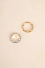 Set de dos anillos dorados, uno con diseño trenzado y otro con incrustaciones de esmalte celeste.