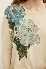Sweater beige de punto con diseño de flores bordadas en tonos celestes y verdes en el frente, de cuello redondo y manga larga.