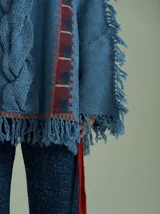 Sweater oversize de lana con diseño de trenza central, detalles en tejido cuadrillé y terminaciones desflecadas. Presenta mangas acampanadas, cuello a la base y aberturas laterales con tiras ajustables.