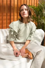 Blusa de tela con estampado vichy en tonos verde pistacho y blanco. Presenta cuello redondo, mangas cortas con tres volados escalonados y puños elásticos. El diseño incluye cierre con botón en la parte posterior.