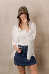 Camisa blanca de calce amplio, confeccionada en tejido liviano con sutiles rayas verticales, cuello clásico, mangas largas con hombros caídos y abotonadura frontal.