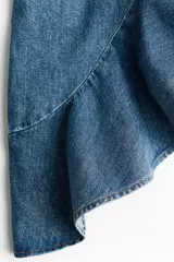 Pollera midi de denim de algodón rígido, con diseño asimétrico, tiro medio, pinzas en la cintura y volado con volumen en el borde inferior.