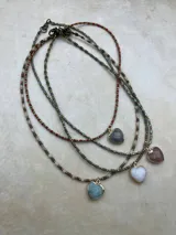 Collar de tres niveles compuesto por cuentas pequeñas de piedra natural y metal, con tres dijes en forma de corazón de piedra natural facetada en tonos rosado, negro y gris, enmarcados en metal dorado.