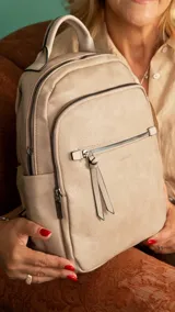 Mochila urbana color beige de símil cuero, con dos bolsillos frontales, bolsillo principal de gran capacidad con dos bolsillos internos con cierre y uno abierto, bolsillos laterales abiertos, asa de mano y correas regulables en galón.