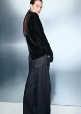 Blazer de terciopelo negro con cuello de solapa, cierre cruzado con botones, bolsillos con solapa en la parte frontal y mangas largas.