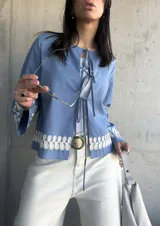 Chaqueta celeste con bordados florales blancos en el ruedo y los puños, con escote redondo y lazos para atar en el frente.