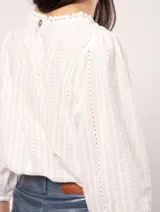 Blusa blanca de algodón con escote redondo, manga tres cuartos y silueta oversized. Presenta bordados y texturas combinadas.