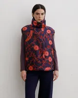 Chaleco puffer con cuello alto y cierre frontal oculto, estampado con diseño floral y de aves en tonos rojos sobre base azul oscuro.
