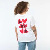 Remera blanca de corte oversize y manga corta, con estampado en la espalda que presenta corazones rojos y la palabra LOVE en letras negras.