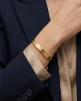 Pulsera tipo esclava rígida de acero con baño de oro, con diseño grabado de patrón geométrico de rombos en toda su superficie.