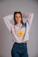 Buzo negro de tejido texturizado con apliques de flores de crochet en colores rosa pálido, amarillo y azul. Tiene cuello redondo y mangas largas.