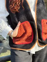 Chaleco negro con interior de corderito, con detalles en color naranja y ribeteado en marrón.