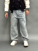 Pantalón de jean estilo baggy de corte ancho y relajado, color azul claro con lavado desgastado. Presenta un bordado en el bolsillo trasero derecho con un diseño de llamas y las siglas SDA.