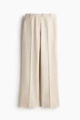 Pantalón sastrero color beige de tiro alto, confeccionado en mezcla de lino y lyocell. Presenta diseño de perneras rectas con pliegues frontales y traseros, bolsillos al bies y trabillas para cinturón.