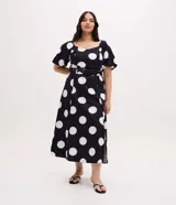 Vestido midi de algodón con estampado de lunares blancos sobre fondo negro. Presenta escote en V, mangas cortas abullonadas, cintura ajustada con cinturón de hebilla y falda con tajo lateral.