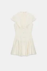 Vestido mini satinado de color blanco, con escote en V pronunciado, mangas cortas casquillo y detalles de botones revestidos en el frente con presillas. Presenta un diseño ajustado en la cintura con costuras estilo corsé y falda corta con vuelo terminada en volante.