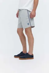 Short de baño oversize gris, con cintura elástica ajustable mediante cordón, bolsillos laterales y detalle de cinta estampada en los laterales.