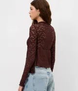 Blusa de encaje color bordó con trama floral y transparencia. Presenta cuello medio, mangas largas ajustadas y un recorte debajo del busto que genera un efecto peplum con volados en el dobladillo.