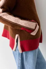 Campera de tejido de punto con cierre frontal, cuello alto y diseño color block en tonos marrón, rosa y rojo. Presenta detalles de trenzas en las mangas y puños y ruedo acanalados.