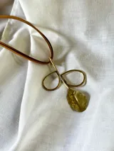 Collar con dije de tijera y hoja de metal dorado, con cordón de cuero marrón.