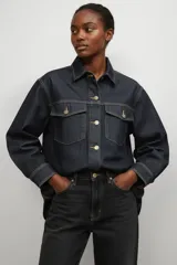 Sobrecamisa de jean en color azul índigo oscuro, con corte holgado, cuello clásico, cierre frontal con botones metálicos y dos bolsillos delanteros con solapa.
