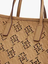 Cartera tote color beige con diseño calado del monograma TH en relieve. Tiene doble asa corta y correa larga extraíble. Incluye cierre magnético y detalles metálicos dorados.