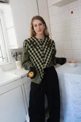 Blusa de algodón con estampado cuadrillé en tonos verde oliva y negro. Presenta cuello redondo, cierre frontal con botones, mangas largas levemente abullonadas y detalles bordados en el canesú.