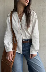 Camisa blanca de manga larga con detalles bordados en las mangas y encaje en el frente y hombros, escote en V con botones frontales.