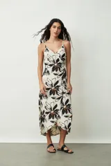 Vestido midi de tirantes finos, con escote en V y diseño cruzado estilo pareo. Presenta un estampado floral grande en tonos negros y naranjas sobre base off-white.