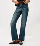 Pantalón de jean corte bootcut con tiro bajo, confeccionado en denim de algodón con lavado dirty que aporta un efecto envejecido. Presenta cierre frontal con botón y cremallera, presillas en la cintura y detalle de tachas metálicas en los bolsillos frontales.