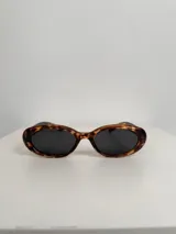 Lentes de sol con armazón ovalado de color negro y cristales tonalidad marrón. Presentan un detalle metálico en forma de estrella en las patillas.