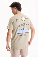 Remera verde claro de corte regular, con manga corta y estampa en la espalda que representa un paisaje de montañas, sol y una ola con la inscripción "est.96".