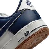 Zapatilla deportiva Nike Air Force 1 '07 LV8, caña baja, con capellada de cuero en colores azul marino y blanco. Presenta el logo Swoosh en azul marino y forro interior afelpado azul. La entresuela es de color crema y la suela exterior es de goma color caramelo.