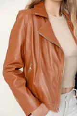 Campera estilo motociclista de cuero color marrón caramelo, con cuello solapa, cierre asimétrico plateado y detalles de broches metálicos.