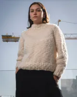 Sweater de cuello redondo tejido a mano en dos agujas, confeccionado en una mezcla de lana merino y seda. Presenta un diseño de punto grueso con detalle de bordado artesanal en color azul.