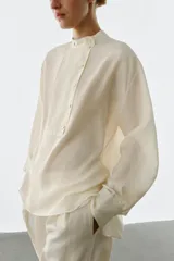Camisa de manga larga confeccionada en seda 100%, con cuello mao y cierre frontal con botones. Presenta un diseño con bajo asimétrico y puños clásicos.