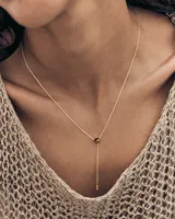 Collar tipo gargantilla en plata de ley con baño de oro de 18k, diseño tipo lazada con una piedra central de ojo de tigre y un colgante en forma de barra fina en el extremo inferior.