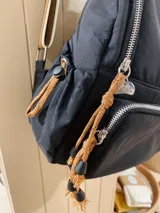 Mochila de nylon color negro con cierre frontal, correas ajustables estampadas con el nombre de la marca y parche bordado decorativo en el frente.